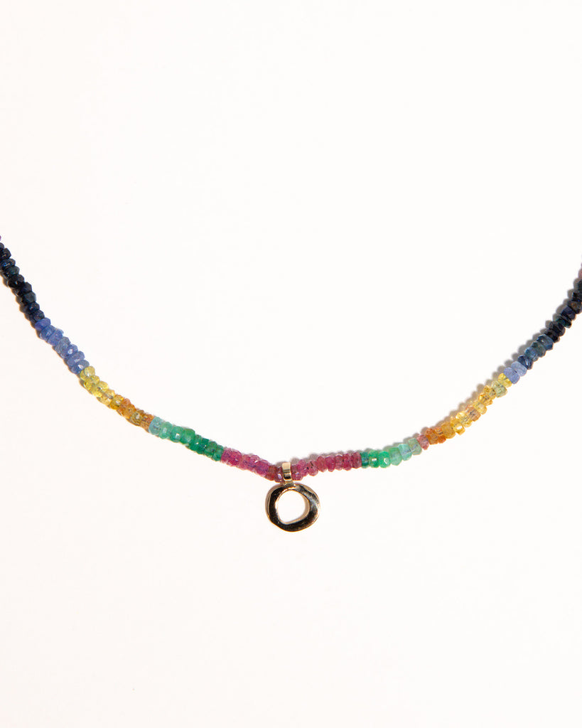 sapphires, emeralds and rubies beaded necklace handstrung on silk thread handcrafted in London with 9ct solid gold organic charm by Maya Magal London